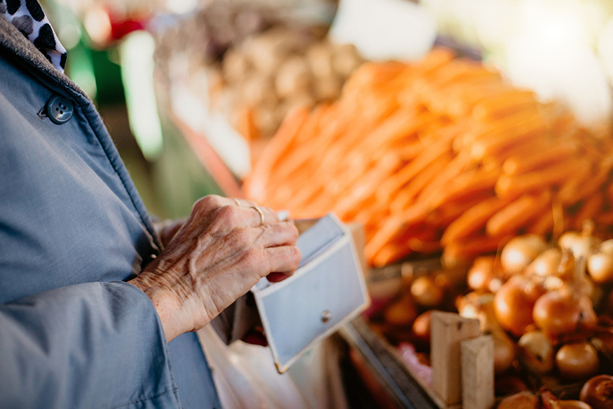 woman looking into a blue wallet near produce at a grocery store. 